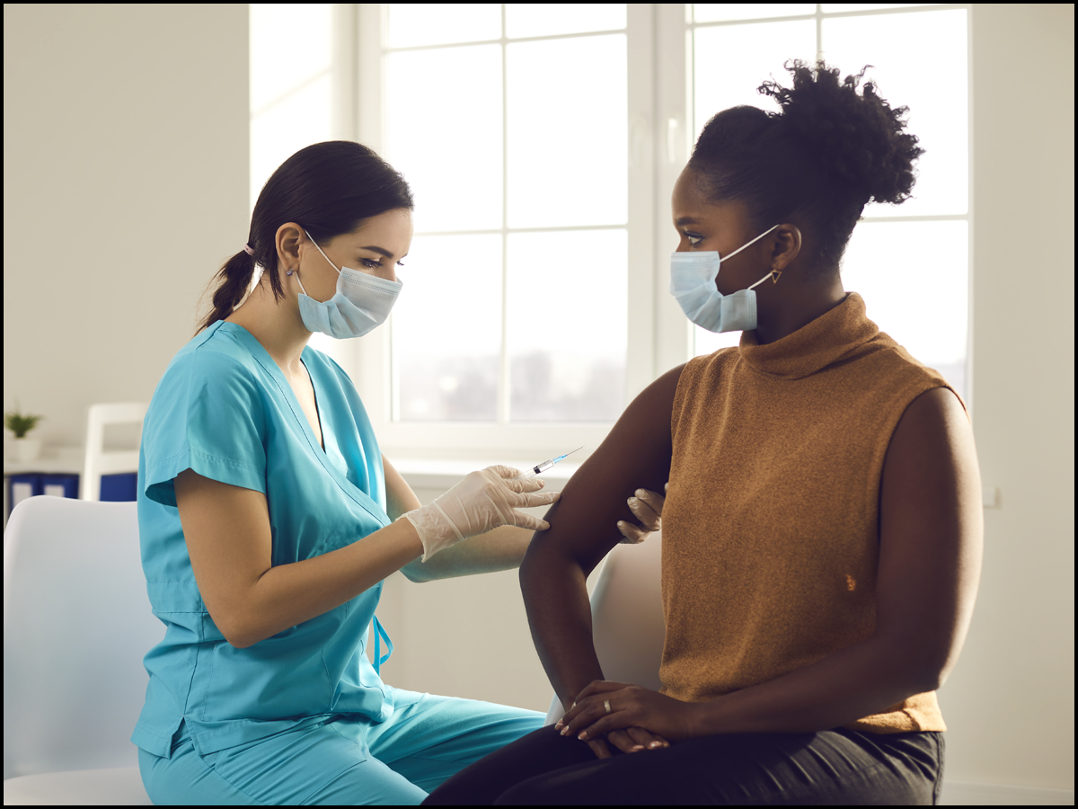 Female presenting person receiving a vaccine in her right arm from a female presenting nurse