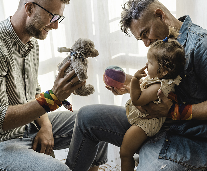 Two fathers playing with their daughter